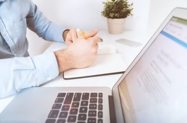 A man making bookkeeping notes in a notebook next to a laptop not knowing the four advantages of outsourcing his bookkeeping.